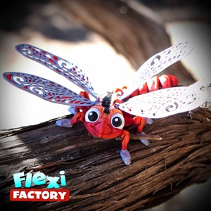 May include: A red and white dragonfly toy with large eyes and articulated wings. The wings are grey with a decorative pattern. The toy is perched on a piece of driftwood. The text "Flexi Factory" is in the lower left corner.