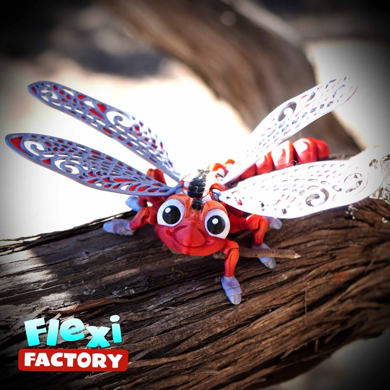May include: A red and white dragonfly toy with large eyes and articulated wings. The wings are grey with a decorative pattern. The toy is perched on a piece of driftwood. The text "Flexi Factory" is in the lower left corner.