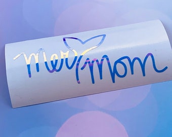 May include: A white vinyl sticker with a blue iridescent mermaid tail and the text "Mermom" in blue iridescent lettering.