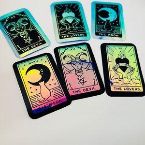 May include: Six holographic tarot cards with black borders and rainbow backgrounds. The cards are: The Devil, The Lovers, The Moon, The Devil, The Moon, and The Lovers.