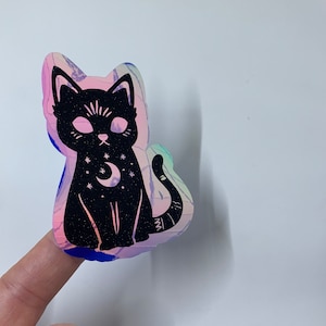 May include: A black cat silhouette sticker with a crescent moon and stars on its chest. The sticker is on a holographic background with pink, blue, and purple colors.