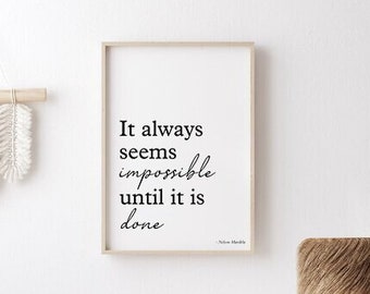 May include: A framed inspirational quote print with the text "It always seems impossible until it is done." The print is hanging on a white wall in a room with a wicker chair, a small table, and a fluffy lamp.