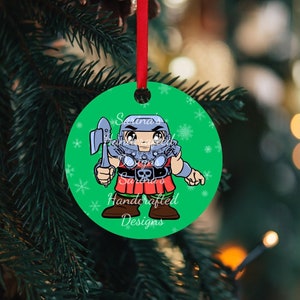 May include: A round green Christmas ornament featuring a cartoon warrior with an axe on one side and the text "Masters of the Universe", "NICHOLAS", and "2023" on the other side. The ornament hangs from a red ribbon and has a snowflake pattern.