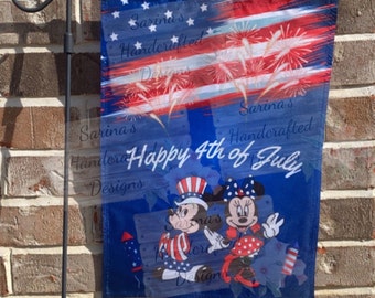 May include: A patriotic garden flag featuring a red, white, and blue design with fireworks and the text "Happy 4th of July." The flag includes illustrations of Mickey and Minnie Mouse in patriotic outfits.