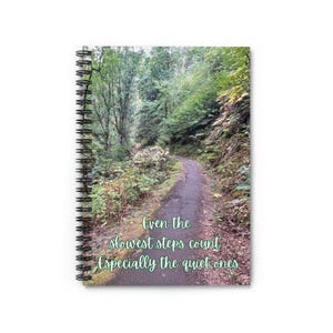 May include: A spiral bound notebook with a green and brown forest path image. The text "Even the slowest steps count Especially the quiet ones" is printed on the front cover.