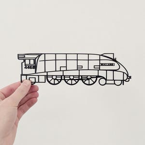May include: A black outline of a train, held by a hand. The train is labelled with the number "4468" and the name "Mallard". The design is a stylized representation of a locomotive, with visible wheels and windows.