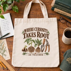 May include: A cream-colored canvas tote bag featuring a brown graphic print of a sprouting plant, a small garden trowel, and pruning shears. The text reads "WHERE CURIOSITY TAKES ROOT" above the illustration and "AG TEACHER" below the design.