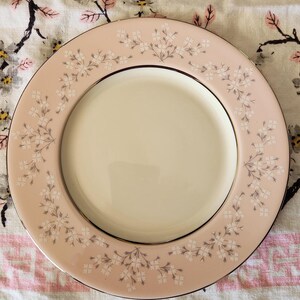 May include: A pink and white floral patterned dinner plate with a gold rim. The plate is made of ceramic and has a smooth, glossy finish.
