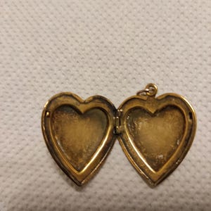 May include: A gold heart-shaped locket with a hinged opening. The locket is open, revealing two empty compartments.