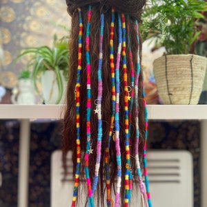 May include: A set of colourful synthetic dreadlocks with gold star and ring charms. The dreadlocks are made of various colours including pink, blue, green, yellow, and white.