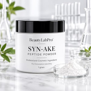 以下が含まれることがあります： 黒い蓋が付いた白いプラスチック製の瓶。ラベルには「BeautyLabPro SYN-AKE PEPTIDE POWDER Professional Cosmetic Ingredient For Formulation Use Only 1 gram」と記載されています。瓶の前には白い粉末が入った小さなガラス皿が置かれています。