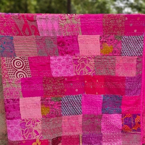 Può includere: Una trapunta patchwork rosa con una varietà di motivi e texture. La trapunta è realizzata con molti pezzi di tessuto diversi cuciti insieme, creando un design unico e colorato.