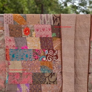 Puede incluir: Una colcha de retazos con una variedad de colores y patrones, incluyendo diseños florales, paisley y geométricos. La colcha está hecha de saris reciclados y está cosida a mano. La colcha es de color marrón, rosa, azul y verde. La colcha está doblada por la mitad y está sobre una superficie de hormigón. El texto "KhatuShyamStore" es visible en la colcha.