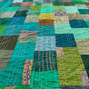 May include: A patchwork quilt made from a variety of green fabrics. The quilt is stitched together with white thread and has a simple, geometric design.