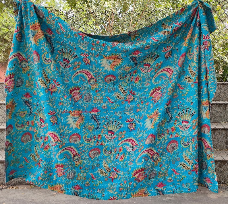 K&ouml;nnte beinhalten: Eine t&uuml;rkisblaue Kantha-Steppdecke mit einem floralen Muster in Rosa-, Gelb- und Gr&uuml;nt&ouml;nen. Die Steppdecke ist aus Baumwolle und handgen&auml;ht.
