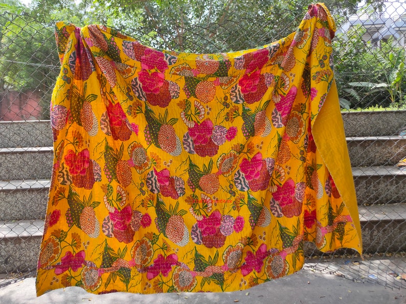 Op de afbeelding: Een gele kantha-deken met een bloemenpatroon in tinten roze, groen en bruin. De deken is gemaakt van katoen en met de hand gestikt.