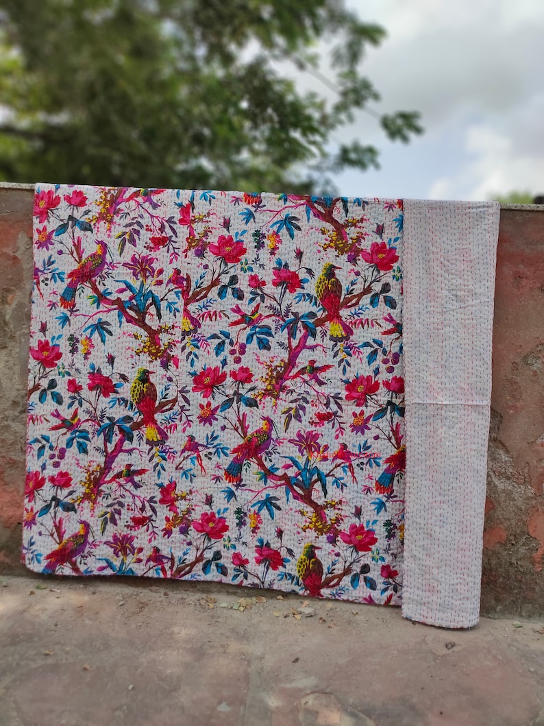 May include: White kantha quilt with a floral and bird pattern. The quilt is made of cotton and has a hand-stitched design. The quilt is perfect for adding a touch of bohemian style to your home.