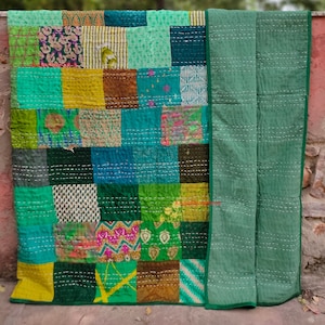 May include: A patchwork quilt with a variety of green, blue, and yellow fabrics. The quilt is made up of squares of different sizes and patterns. The quilt is edged with a solid green fabric.