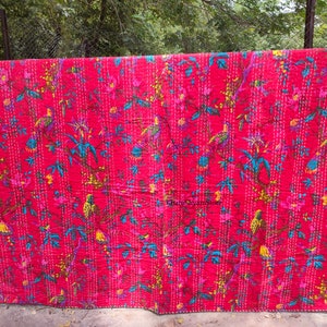 May include: A red kantha quilt with a floral and bird pattern. The quilt is hand-stitched and features a variety of colors, including pink, blue, yellow, and green.