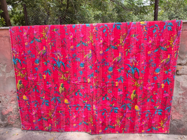 May include: A red kantha quilt with a floral and bird pattern. The quilt is hand-stitched and features a variety of colors, including pink, blue, yellow, and green.