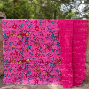May include: A pink kantha quilt with a floral and bird print. The quilt is folded in half and has a plain pink back.