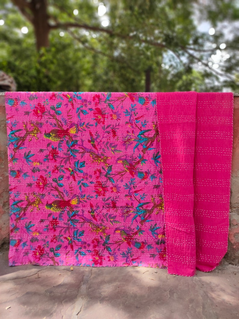 May include: A pink kantha quilt with a floral and bird print. The quilt is folded in half and has a plain pink back.