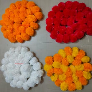 Puede incluir: Cuatro arreglos florales circulares hechos de pétalos densos y rizados. Un grupo es de color naranja brillante, otro rojo intenso, otro blanco nítido y el cuarto es una mezcla de amarillo y naranja. Cada pieza presenta una superficie redondeada.