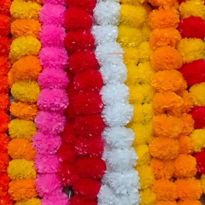 Könnte beinhalten: Eine Sammlung vertikaler Girlanden aus künstlichen Ringelblumen in leuchtenden Farben wie Orange, Gelb, Pink, Rot und Weiß. Jeder Strang besteht aus zahlreichen dicht gepackten, kugelförmigen und gerüschten Blütenköpfen in Reihen.