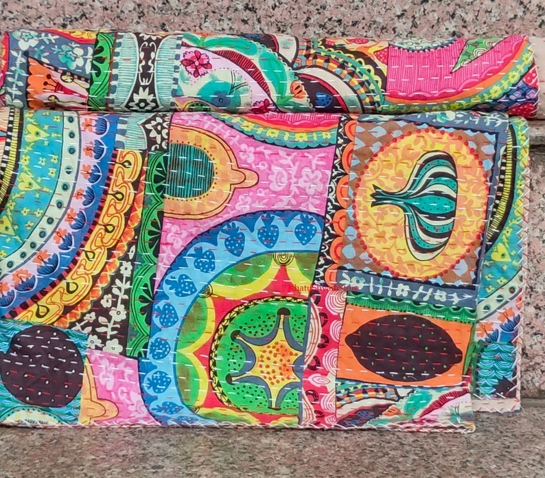 Puede incluir: Una colcha de retazos colorida con una variedad de patrones, incluyendo dise&ntilde;os de paisley, florales y geom&eacute;tricos. La colcha est&aacute; hecha de tela de algod&oacute;n y est&aacute; cosida a mano. La colcha est&aacute; doblada por la mitad y est&aacute; sobre una superficie de piedra.