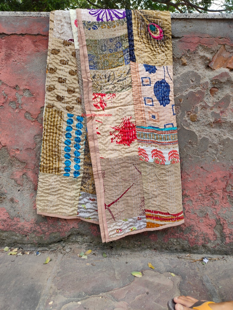 May include: A patchwork quilt made from repurposed fabric scraps. The quilt is beige with brown, blue, red, and green accents. The quilt is hand-stitched and has a unique, rustic look.