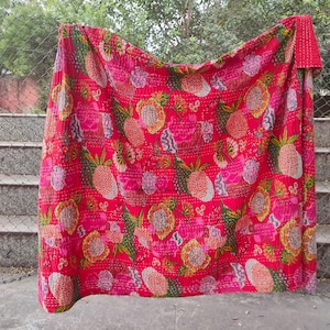 Op de afbeelding: Een rode kantha-deken met een bloemenpatroon met roze, gele en groene bloemen. De deken is gemaakt van katoen en met de hand gestikt.