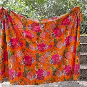 Op de afbeelding: Een kantha-deken met een bloemenpatroon in tinten roze, groen en oranje. De deken is gemaakt van katoen en met de hand gestikt.