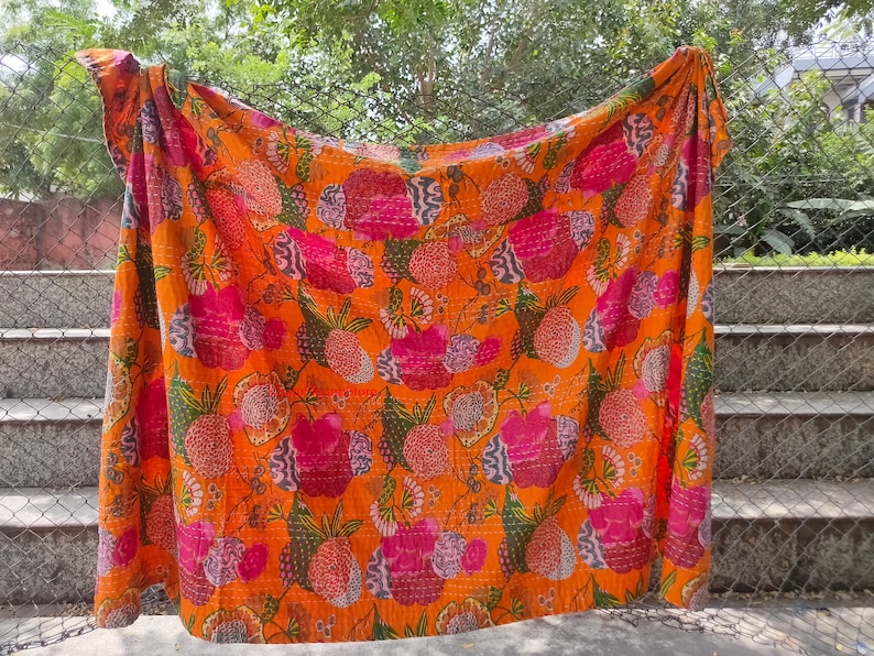 Op de afbeelding: Een kantha-deken met een bloemenpatroon in tinten roze, groen en oranje. De deken is gemaakt van katoen en met de hand gestikt.