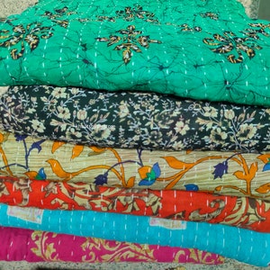 Könnte beinhalten: Ein Stapel bunter Kantha-Steppdecken mit floralen und Paisley-Mustern. Die Decken sind aus recycelten Saris hergestellt und handgenäht.
