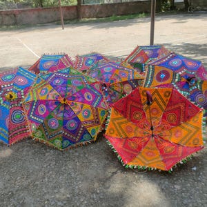 Könnte beinhalten: Eine Sammlung farbenfroher, dekorativer Regenschirme mit aufwendigen geometrischen Mustern. Die Regenschirme weisen eine Vielzahl von Farben auf, darunter Blau, Rosa, Gelb und Orange. Jeder Schirm hat ein einzigartiges Design mit Perlenbesatz.