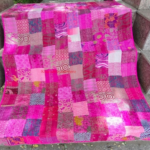 May include: A pink and purple patchwork quilt with a variety of patterns and textures. The quilt is made of recycled saris and is hand-stitched.