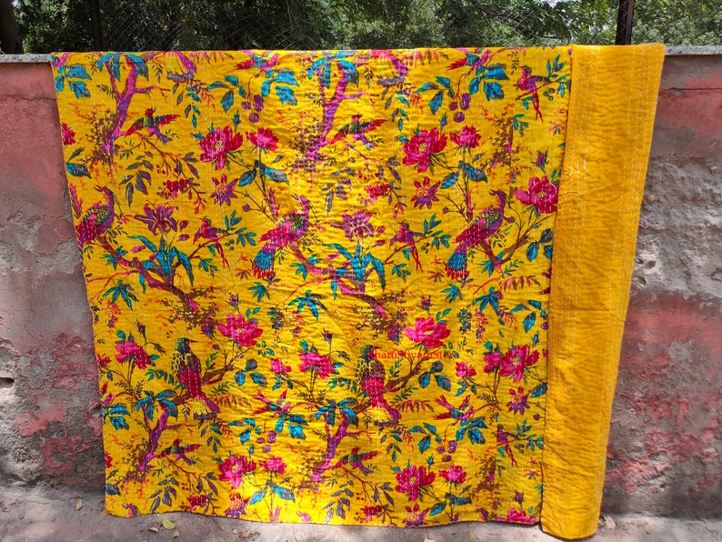 May include: A yellow kantha quilt with a floral and bird pattern. The quilt is made of cotton and is hand-stitched. It is a traditional Indian textile.