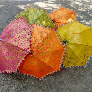 Könnte beinhalten: Eine Sammlung bunter, offener Sonnenschirme. Die Sonnenschirme sind in Pink, Orange, Gelb und Grün gehalten und mit goldenen Blumenmustern versehen. Jeder Sonnenschirm hat eine dekorative Fransen und einen blauen Griff.