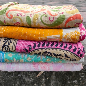 May include: A stack of five colorful, patterned quilts. The top quilt has a beige background with orange, green, and pink paisley designs. The quilts below are yellow, pink, teal, and light pink, each with unique patterns and stitched details.