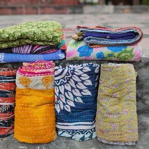 May include: A collection of colorful, patterned kantha quilts. The quilts are stacked and rolled, showcasing various designs including floral, leaf, and geometric patterns in shades of blue, green, yellow, orange, and pink. The image conveys a handcrafted, textile theme.