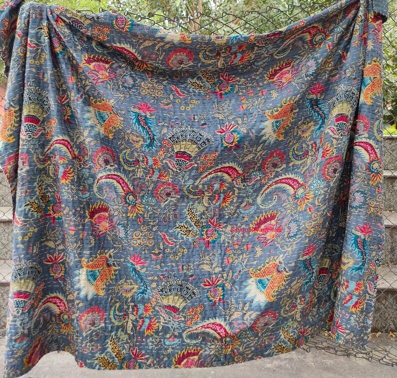 K&ouml;nnte beinhalten: Eine blaue Kantha-Steppdecke mit einem floralen Muster in Rot-, Gelb- und Gr&uuml;nt&ouml;nen. Die Steppdecke ist aus Baumwolle und handgen&auml;ht.