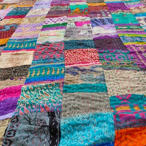May include: A colorful patchwork quilt made from a variety of fabrics. The quilt is made up of squares of different colors and patterns, including floral, paisley, and geometric designs. The quilt is hand-stitched and has a rustic, vintage look.
