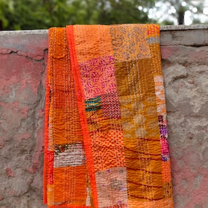May include: A patchwork quilt with a variety of orange, brown, and pink fabrics. The quilt is hand-stitched and has a unique, rustic look.