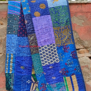 May include: A blue patchwork quilt with various patterns and colors, including purple, green, and gold. The quilt is made of recycled saris and is hand-stitched.