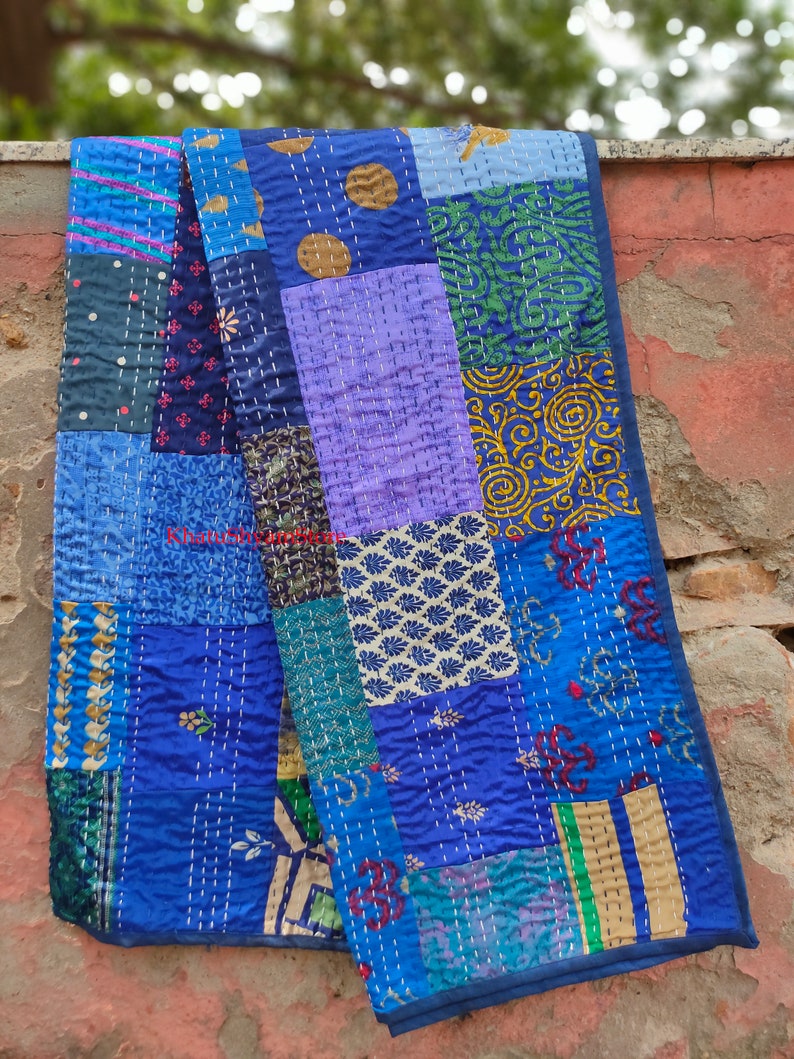 May include: A blue patchwork quilt with various patterns and colors, including purple, green, and gold. The quilt is made of recycled saris and is hand-stitched.