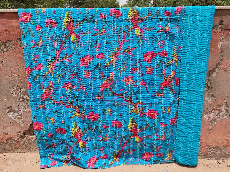May include: A blue kantha quilt with a floral and bird pattern. The quilt is made of cotton and is hand-stitched. It is a traditional Indian textile.
