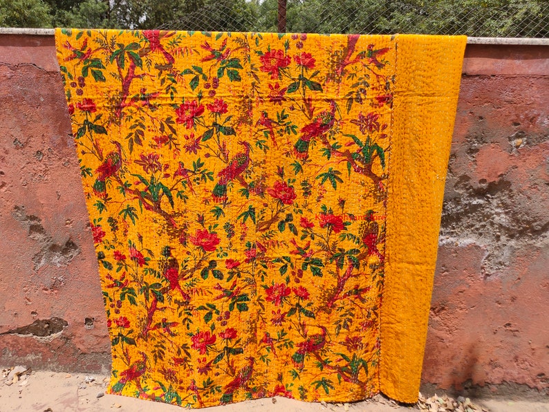 May include: A yellow kantha quilt with a floral and bird pattern. The quilt is made of cotton and is hand-stitched. It is a traditional Indian textile.