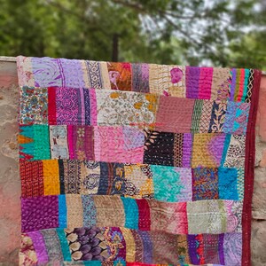 May include: A colorful patchwork quilt made from repurposed fabric scraps. The quilt is made up of squares of different colors and patterns, including floral prints, paisley designs, and geometric shapes. The quilt is stitched together with a running stitch, and the edges are finished with a simple hem.