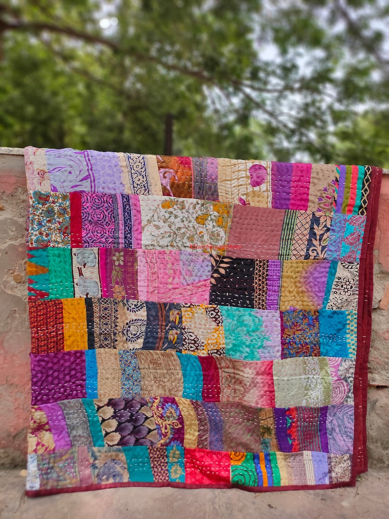 May include: A colorful patchwork quilt made from repurposed fabric scraps. The quilt is made up of squares of different colors and patterns, including floral prints, paisley designs, and geometric shapes. The quilt is stitched together with a running stitch, and the edges are finished with a simple hem.