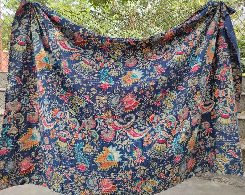 K&ouml;nnte beinhalten: Eine blaue Kantha-Steppdecke mit einem floralen Muster in Rosa-, Gelb- und Gr&uuml;nt&ouml;nen. Die Steppdecke ist aus Baumwolle und hat ein handgesticktes Design.